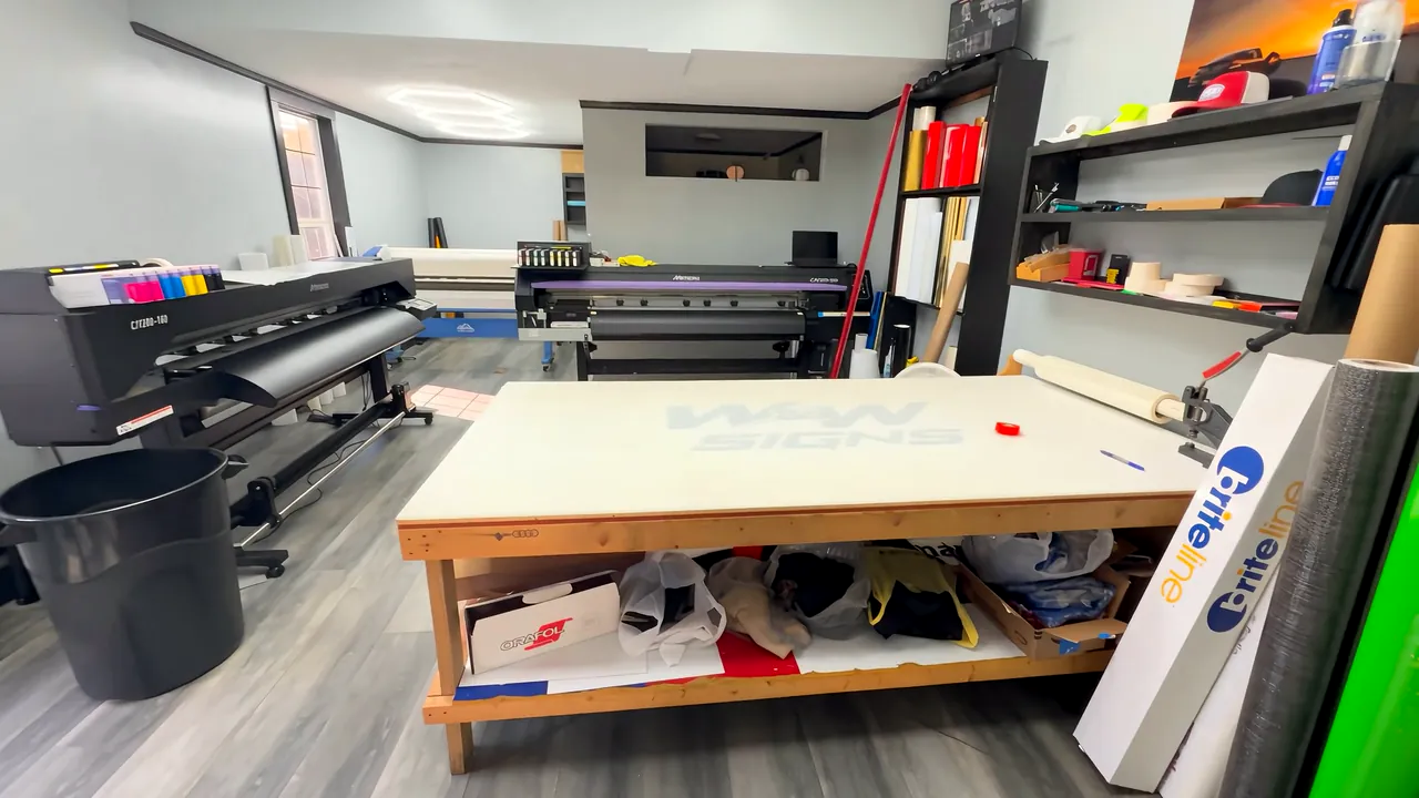 The W&W Signs print floor, with a wide-format printer, a work table and rolls of vinyl on the shelves