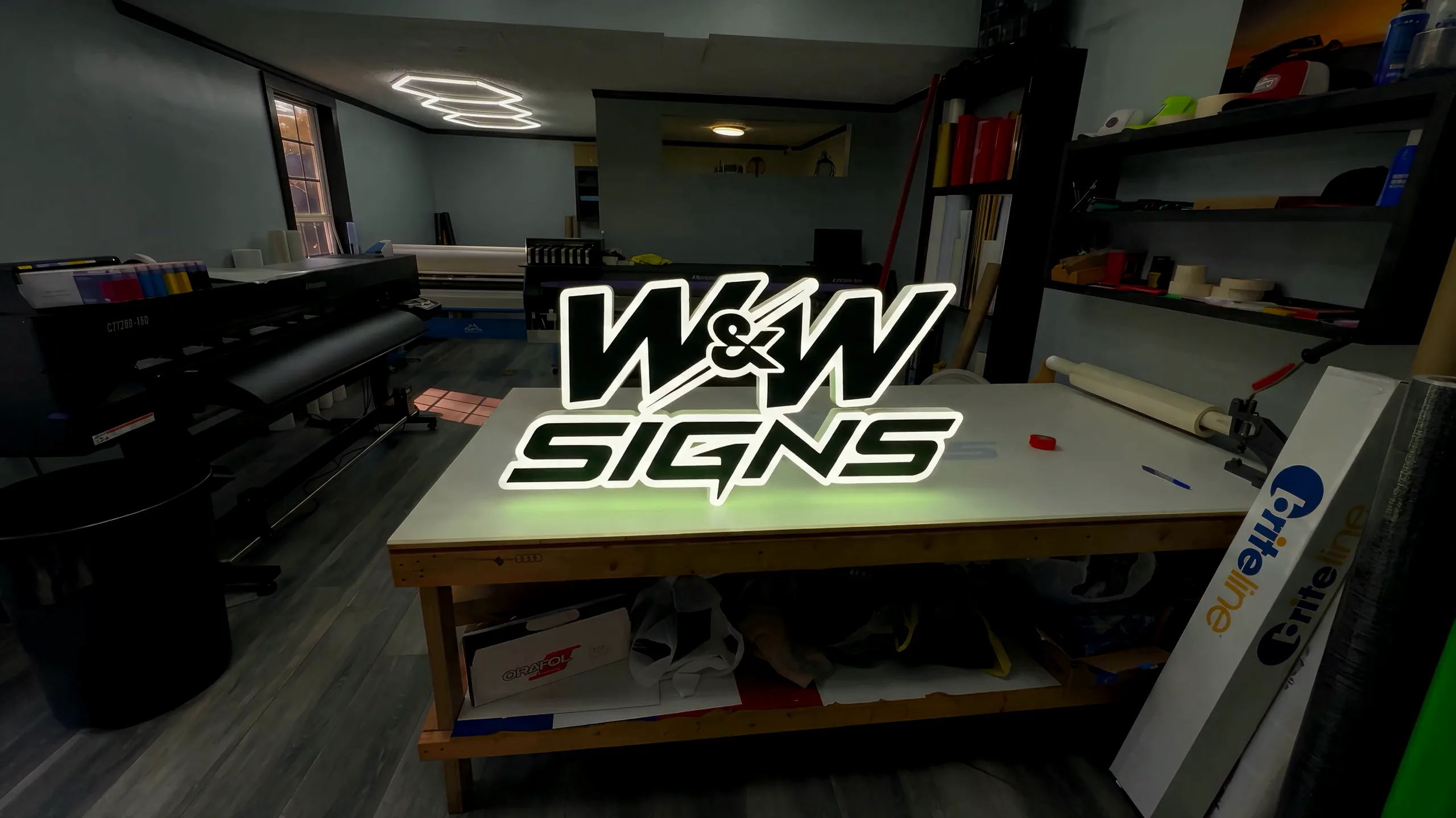 The W&W Signs print floor in Athens, GA, with the W&W Signs logo lit up on the work table